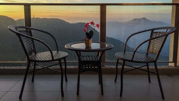 A balcony with wicker chairs and a small table, overlooking a mountainous landscape during sunset. - Sky D'Mont Suites (Genting Highlands)