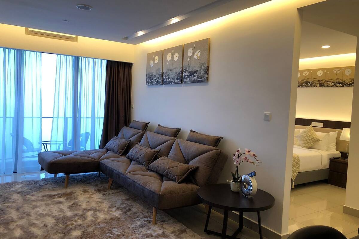 A modern living room with a sofa, a round coffee table, and a view of a bedroom.