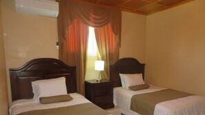 Two single beds with wooden headboards, a nightstand with a lamp, and a window with curtains.