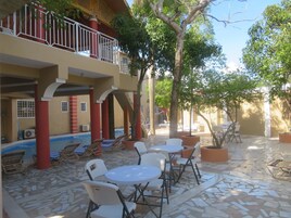 Un patio con mobiliario exterior, piscina y un área cubierta con pilares rojos.