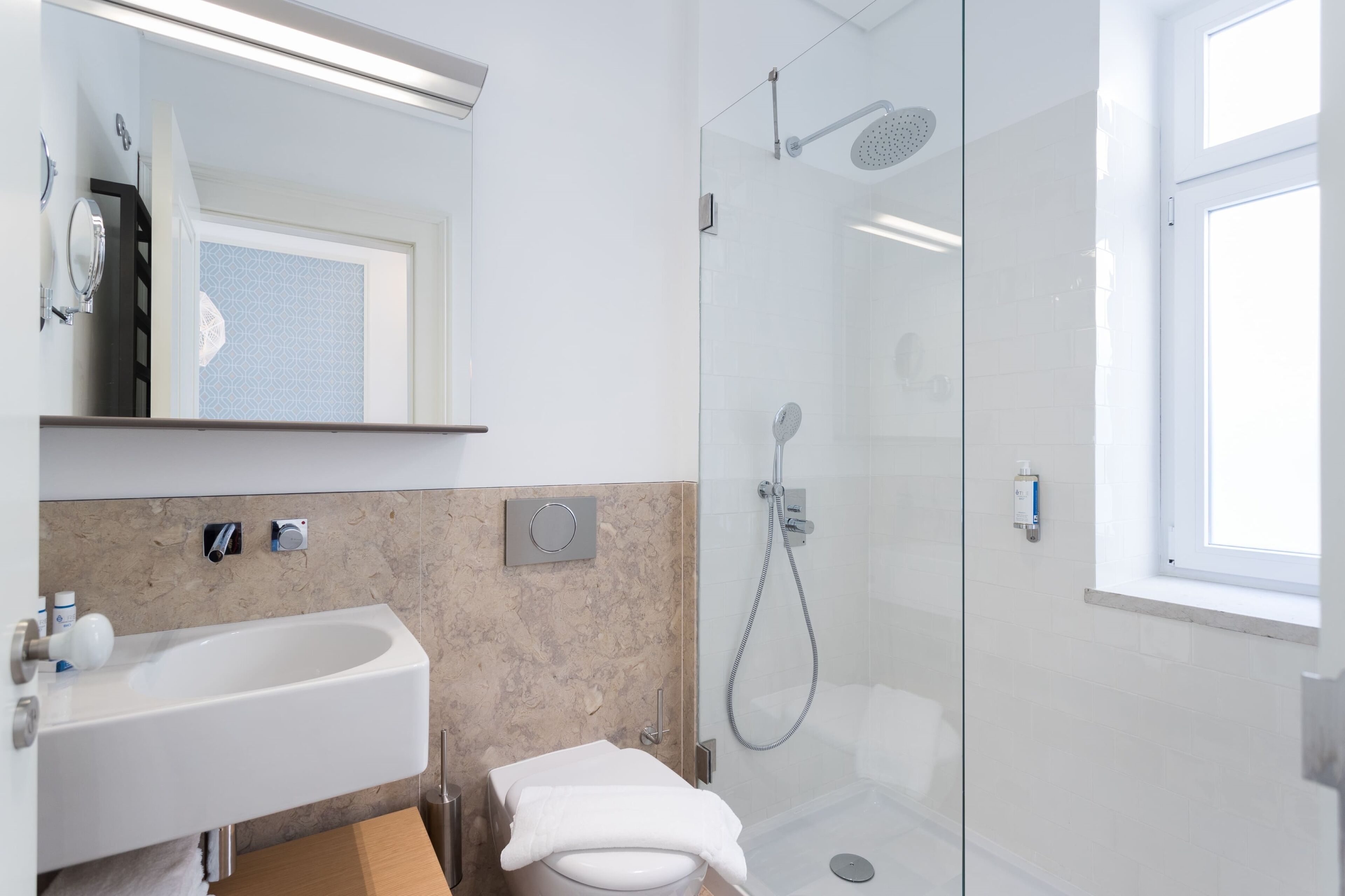 Un baño moderno con ducha envuelta en cristal, un lavabo blanco y un espejo sobre él.