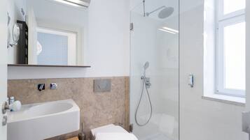 Un baño moderno con ducha envuelta en cristal, un lavabo blanco y un espejo sobre él.