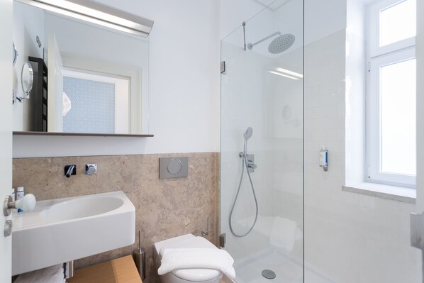 Un baño moderno con ducha envuelta en cristal, un lavabo blanco y un espejo sobre él.