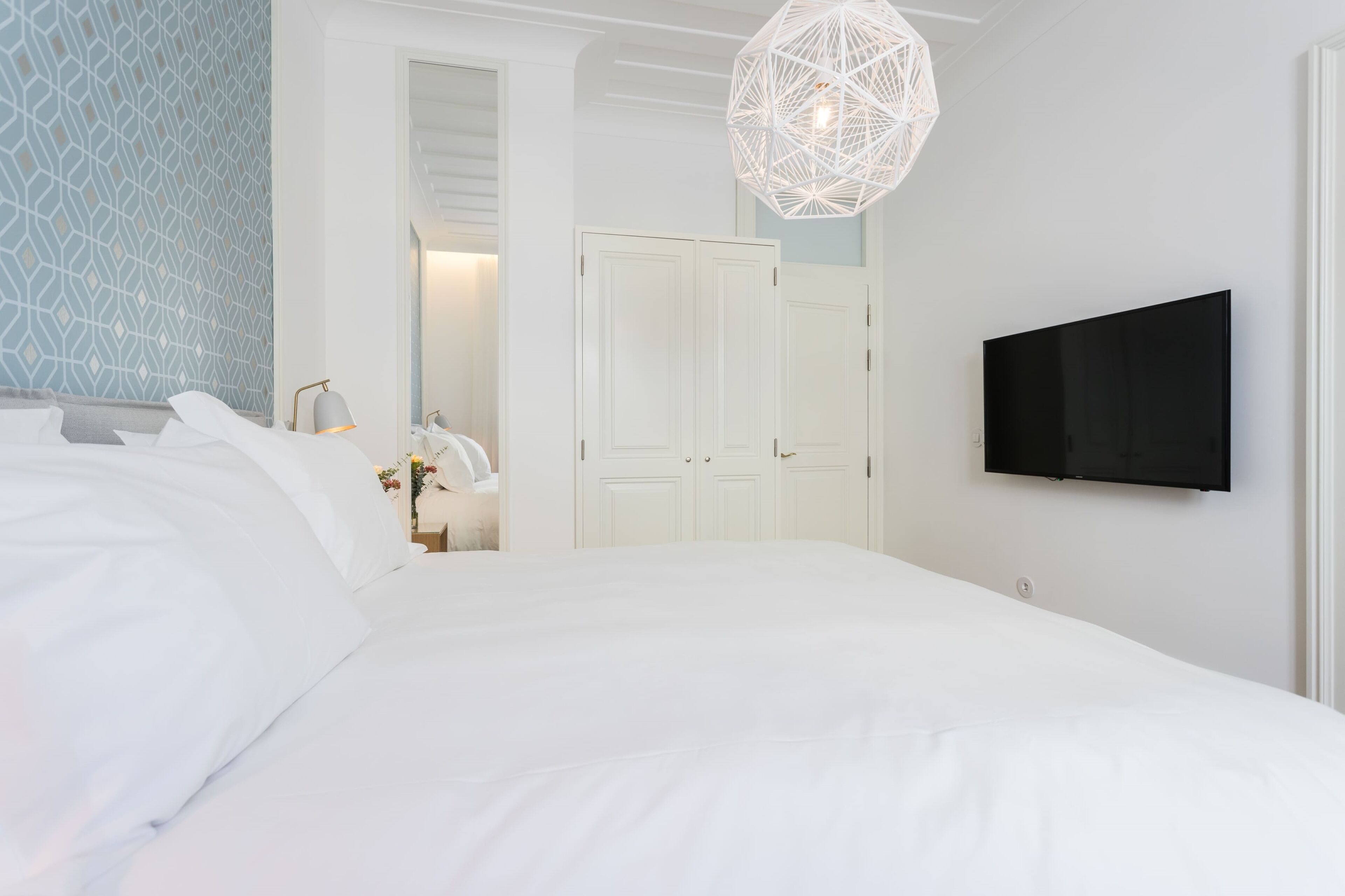 Un dormitorio con una cama grande, un televisor montado en la pared y una lámpara con un diseño geométrico.