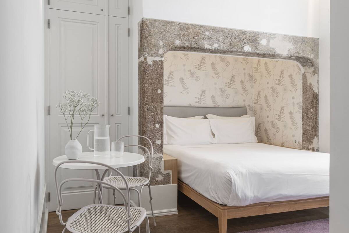 Une chambre à coucher avec un lit, une petite table et des chaises, une armoire blanche et un mur décoratif.