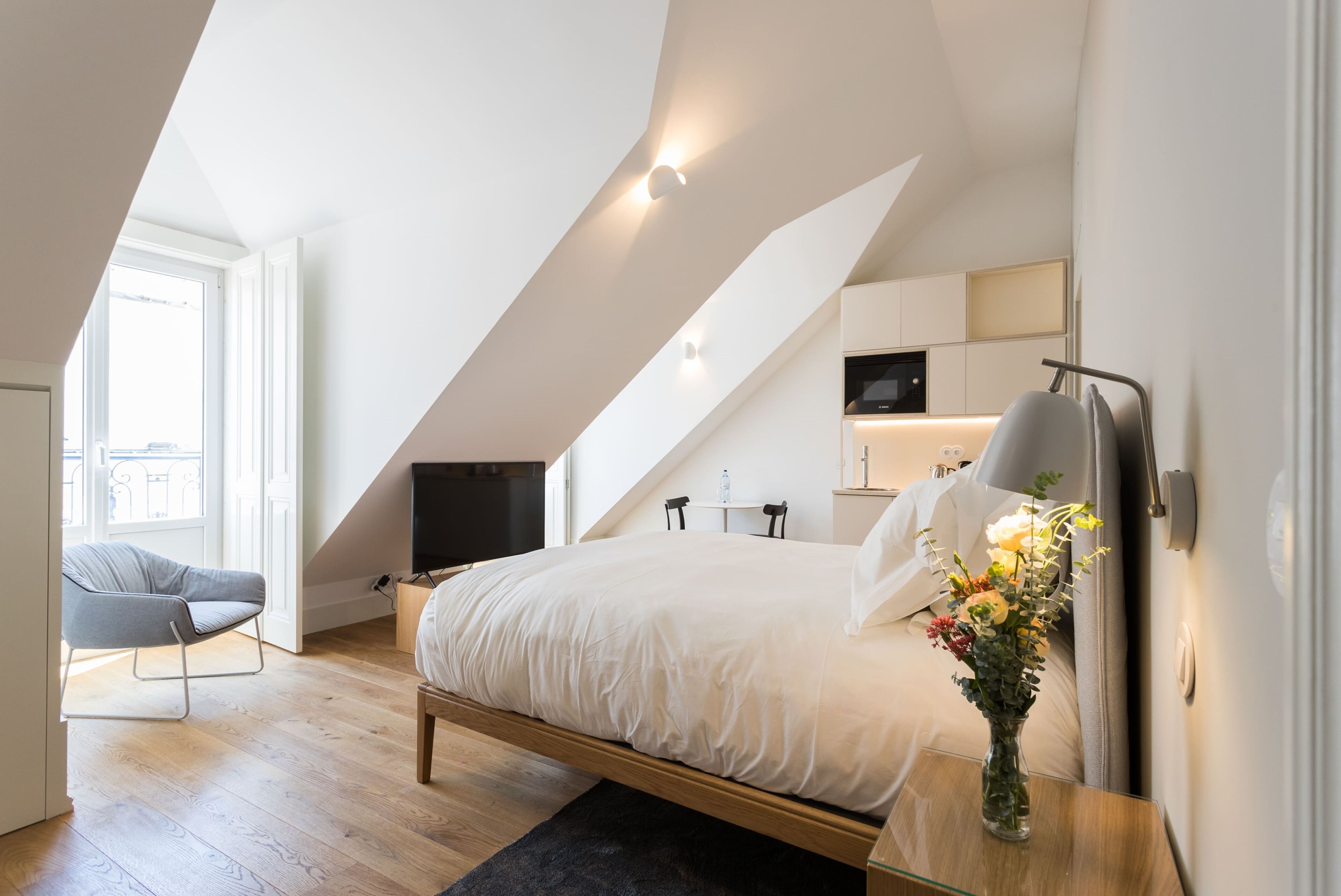 Een moderne slaapkamer met een schuine plafond, een bed, een stoel, een bureau en een televisie.