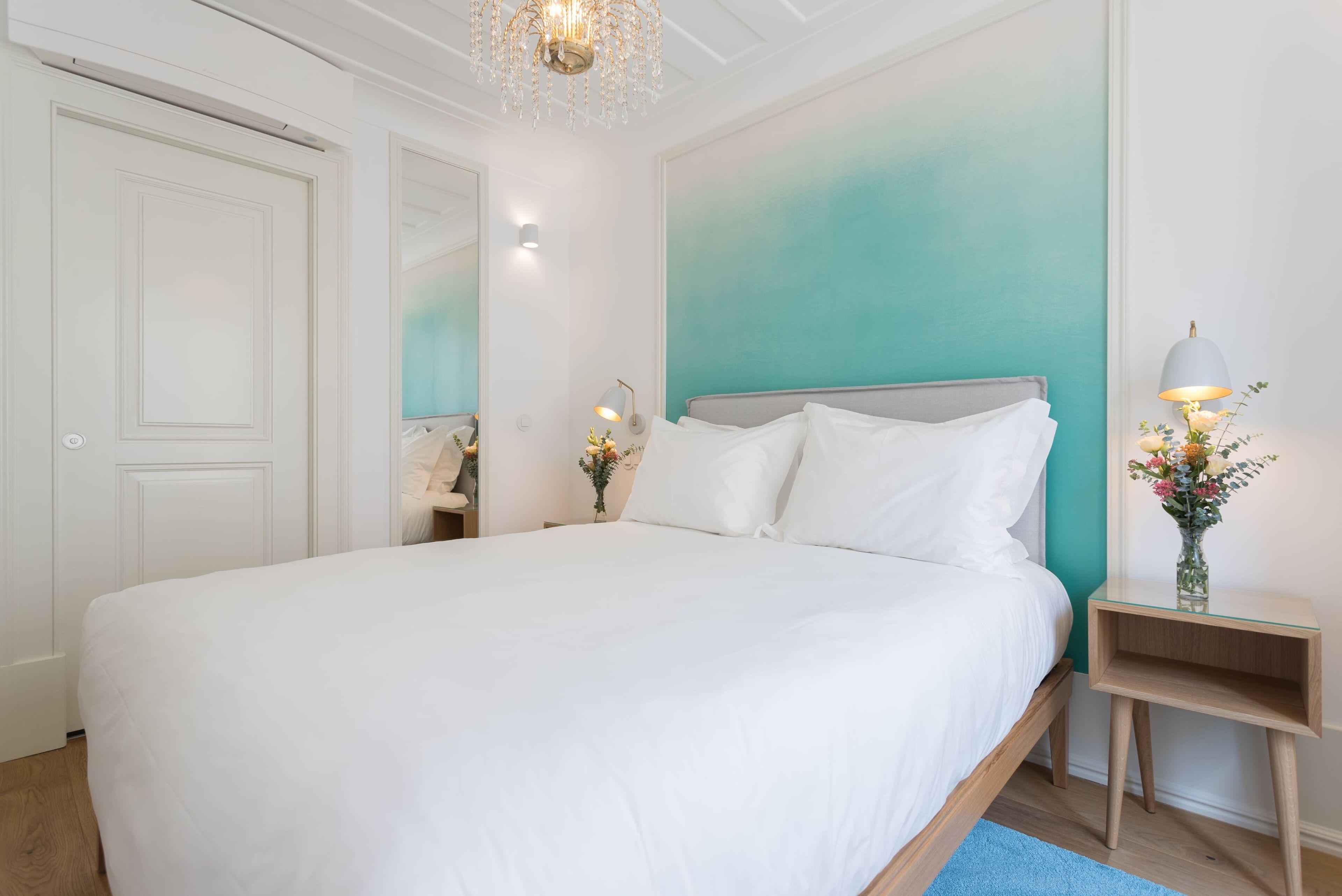 A bedroom with a large bed, a nightstand with a lamp, and a mirror.