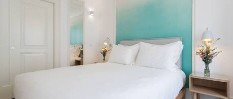 A bedroom with a large bed, a nightstand with a lamp, and a mirror.