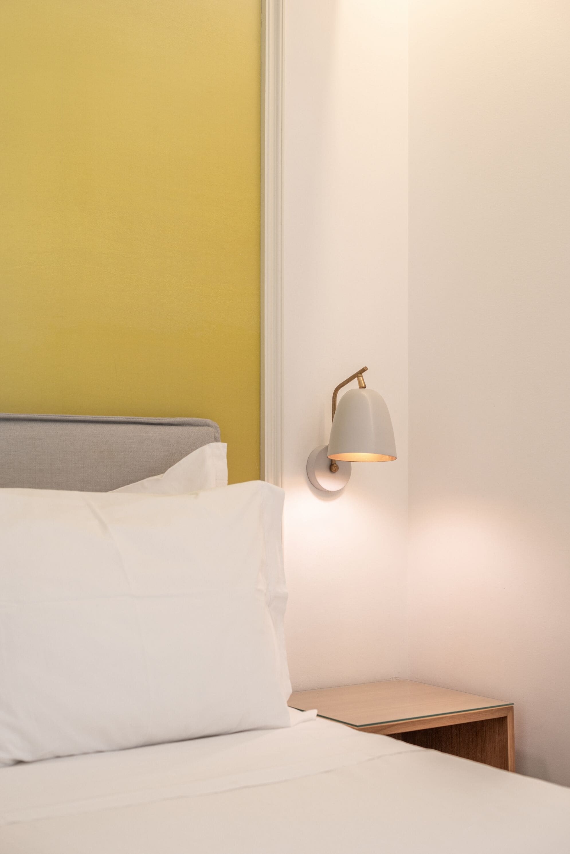 A bed with white bedding, a gray headboard, and a nightstand with a wooden side table.