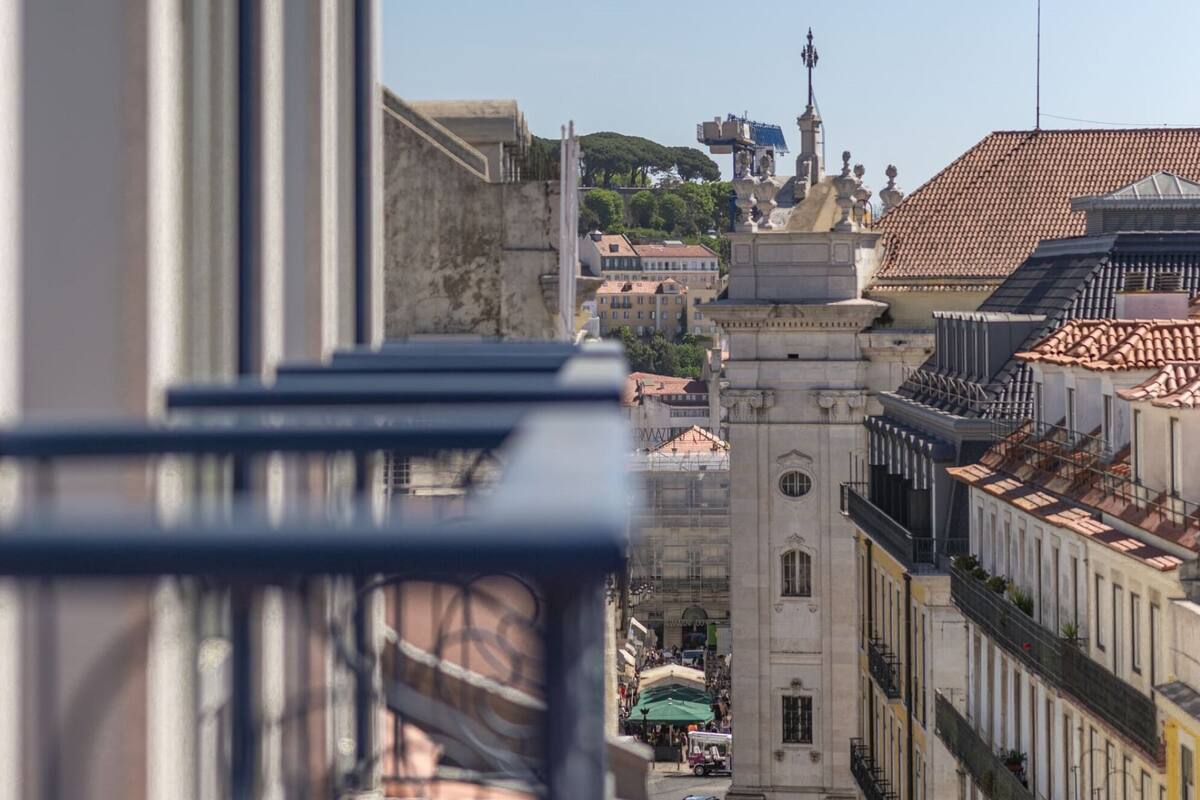 Une vue depuis un balcon donnant sur un paysage urbain, avec des bâtiments historiques et un ciel dégagé.