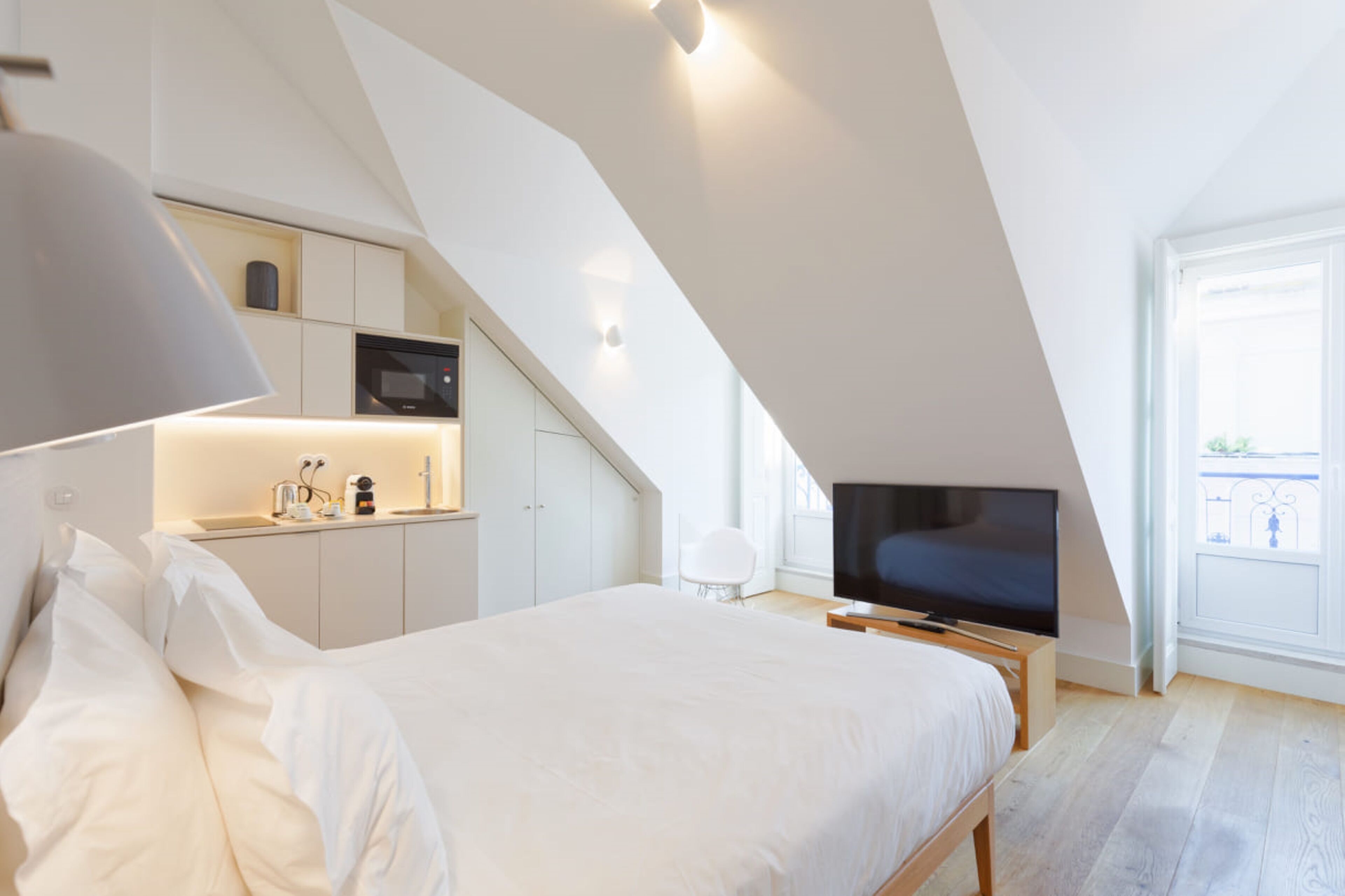 Een moderne slaapkamer met een groot bed, een televisie en een kitchenette in een kamer met een schuine kap.