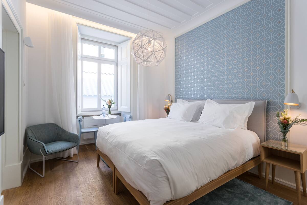 Une chambre à coucher avec un grand lit, une chaise, une petite table et une lampe fixée au mur.