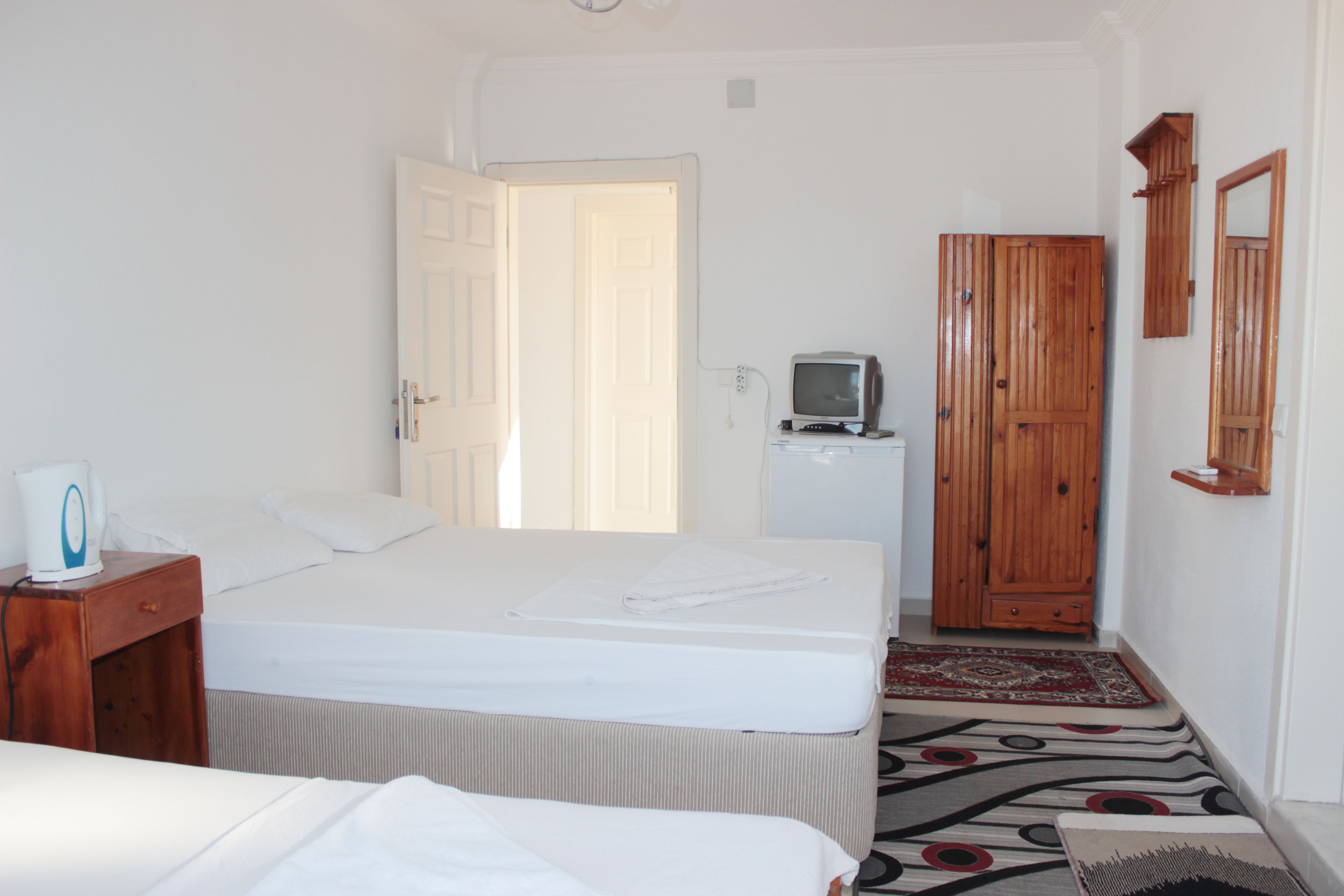 A hotel room with a bed, a small TV, a wooden wardrobe, and a nightstand with a lamp.