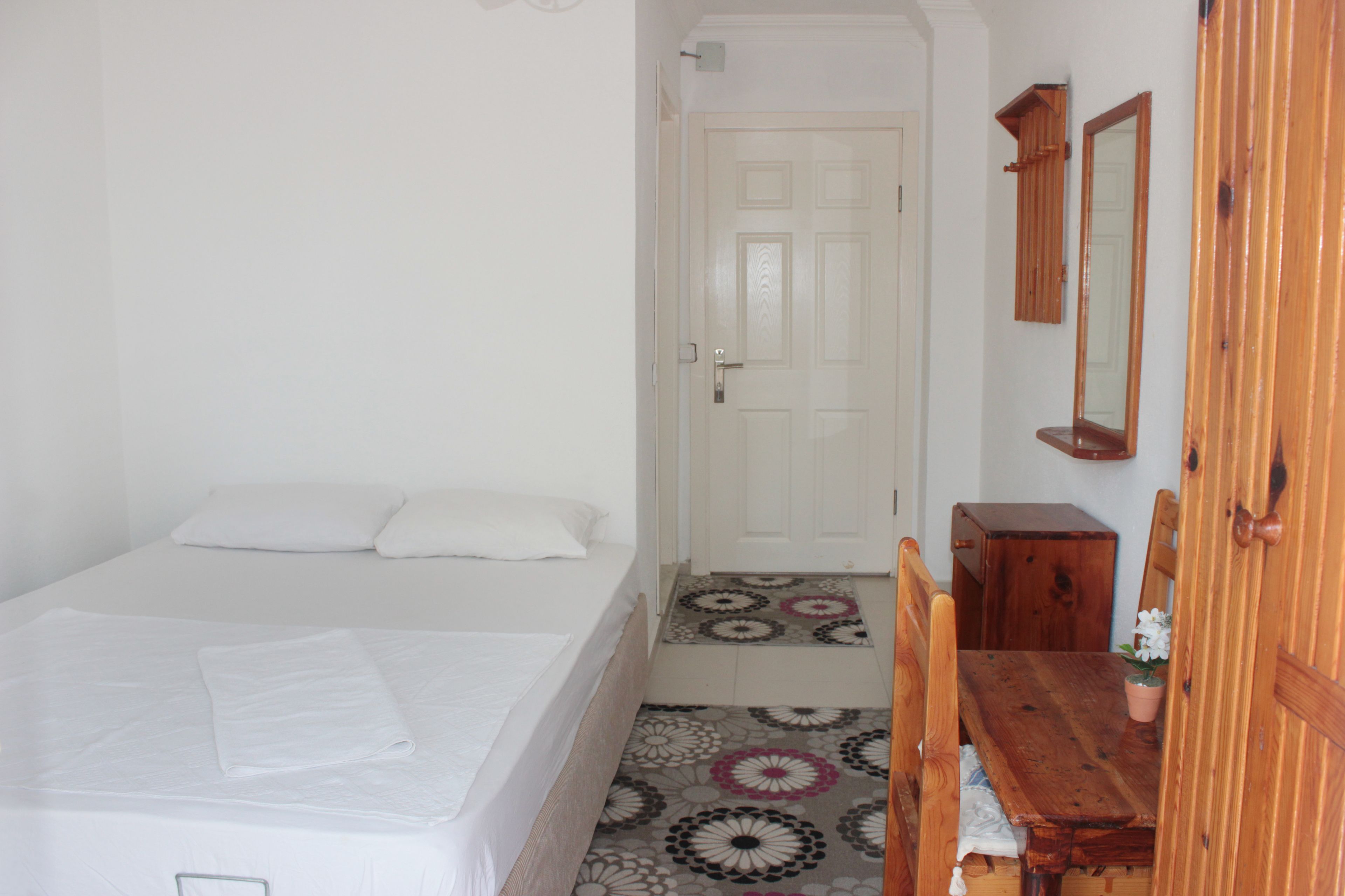 A bedroom with a bed, a wooden dresser, a mirror, and a door.