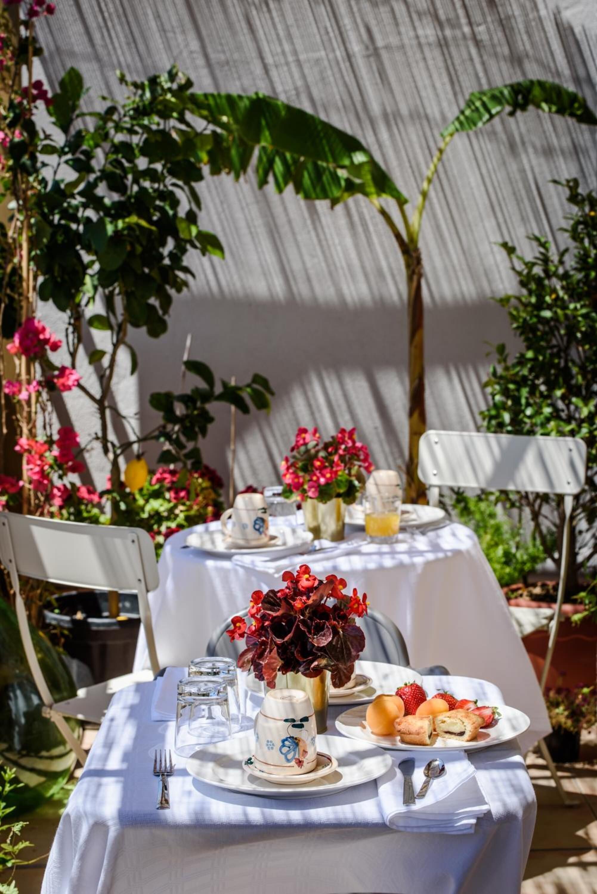 A table set for breakfast with a white tablecloth, plates of food, and a vase of flowers.