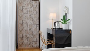 Ein Hotelzimmer mit einer Wand aus Holzbuchstaben, einem schwarzen Schreibtisch mit Lampe, einer weißen Orchidee und einem Bett mit weißer Decke.