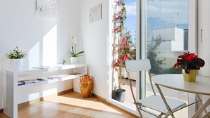 Ein helles Zimmer mit Holzboden, weißen Möbeln, einem großen Fenster mit Blick und Topfpflanzen.