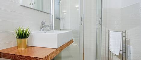 A modern bathroom with a glass shower enclosure, a wooden vanity, and a white sink.