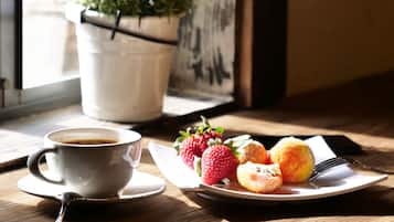 A cup of coffee, strawberries, and pastries on a table near a window with a plant.