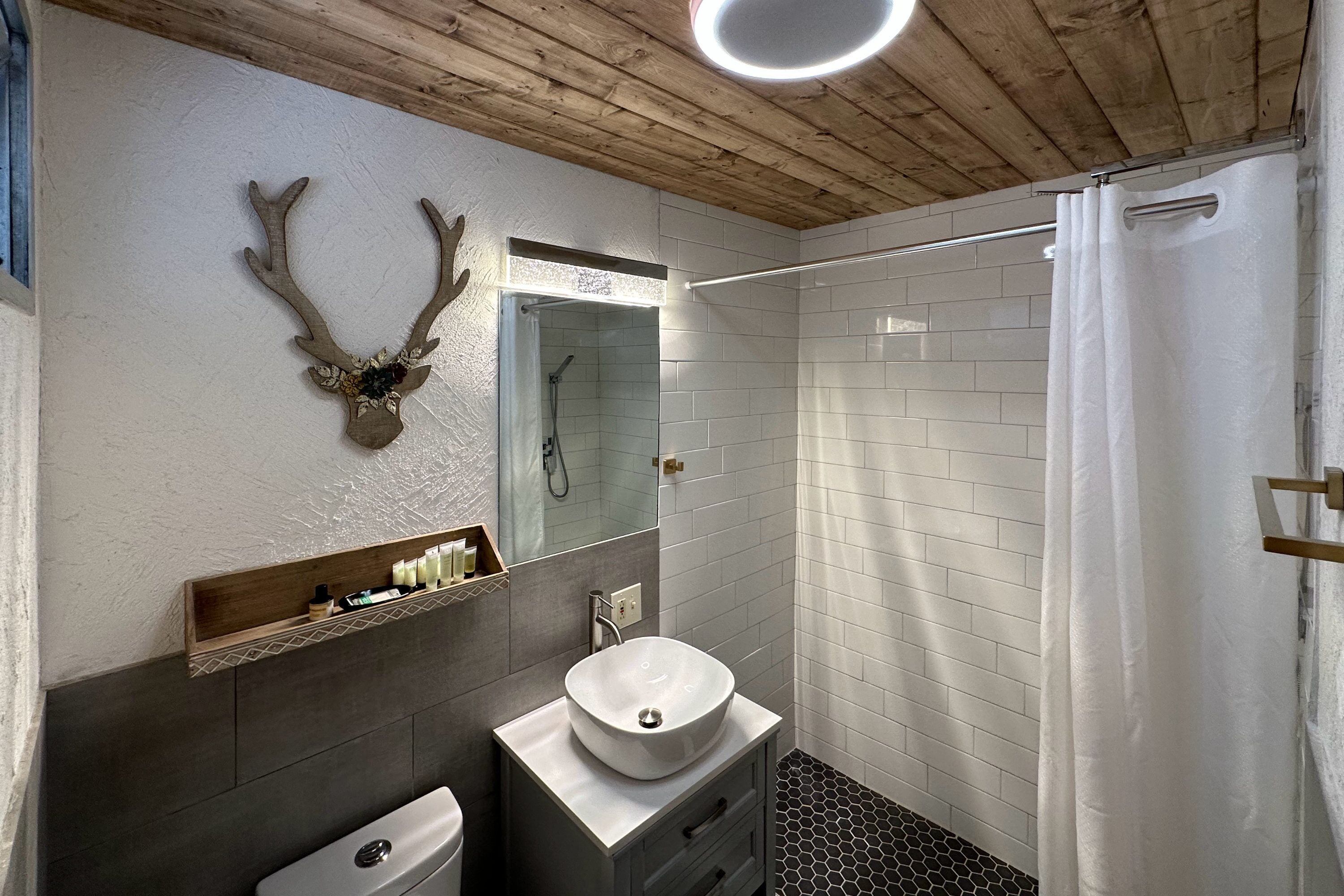 A bathroom with a wooden ceiling, a white sink, a mirror, and a shower.