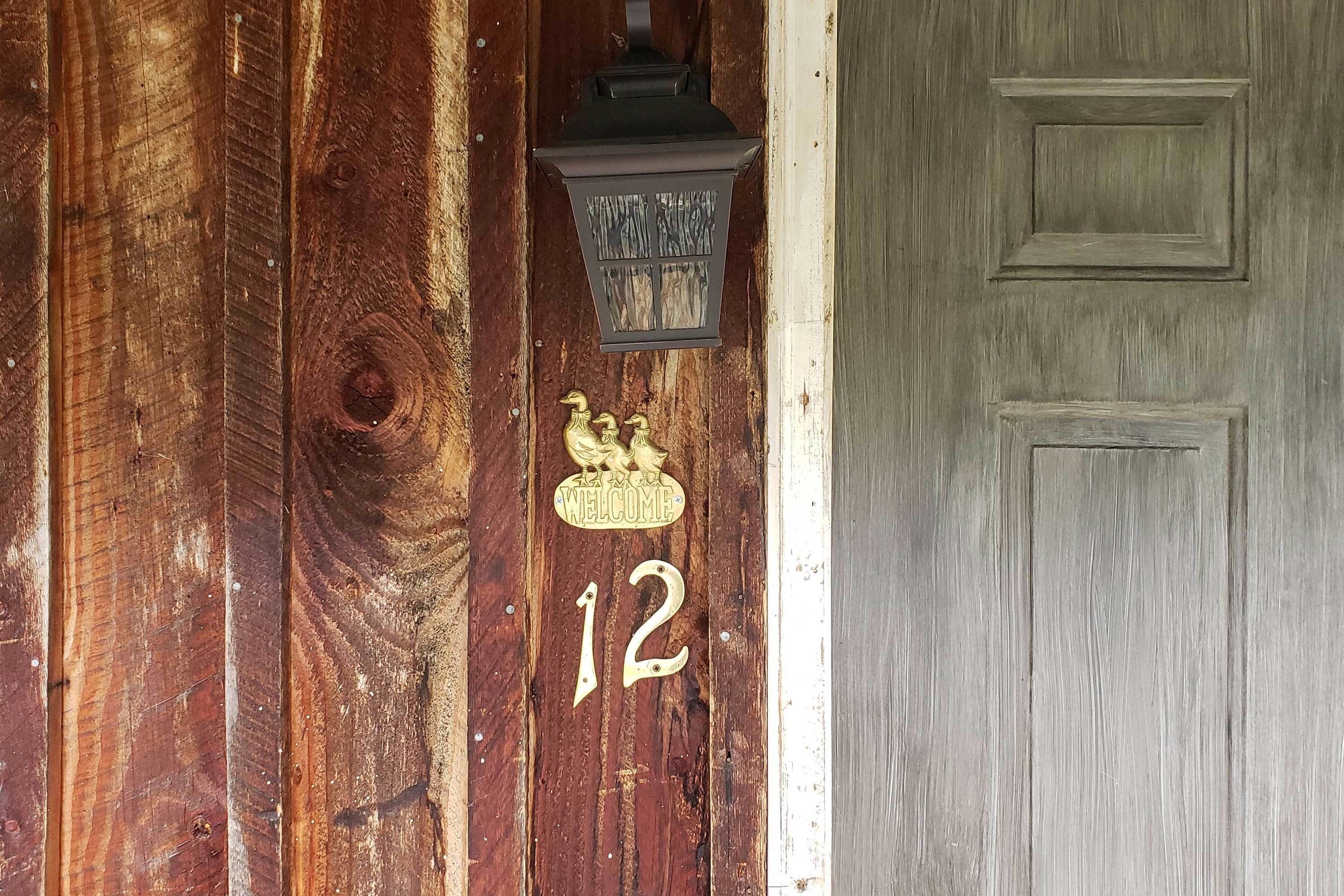 A wooden door with a brass number '12' and a brass 'Welcome' sign above it.