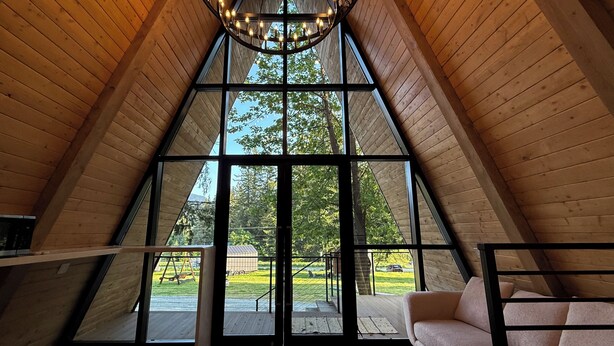 A high-ceilinged room with a large window, a sofa, and a chandelier. - Paradise Village Hotel (Ashford)