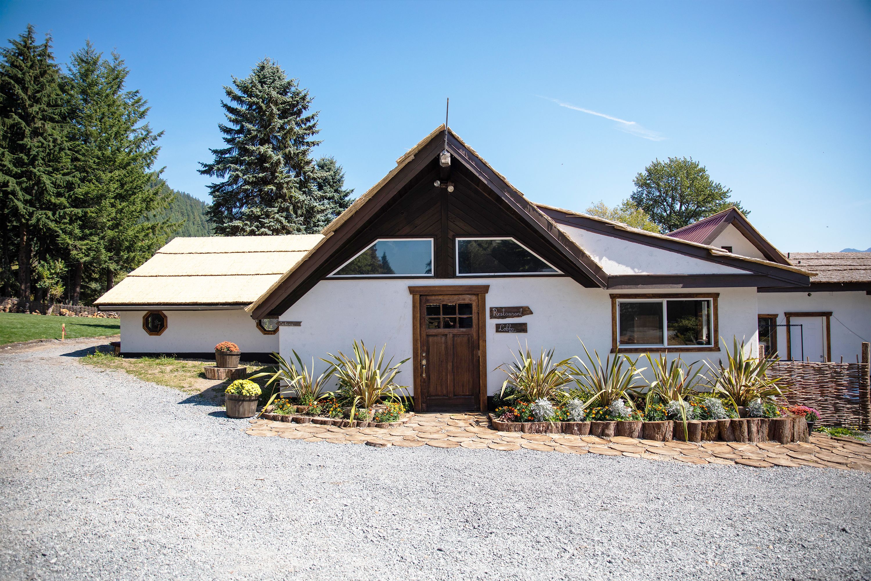 A two-story house with a wooden front door, a small porch with potted plants, and a gravel driveway.
