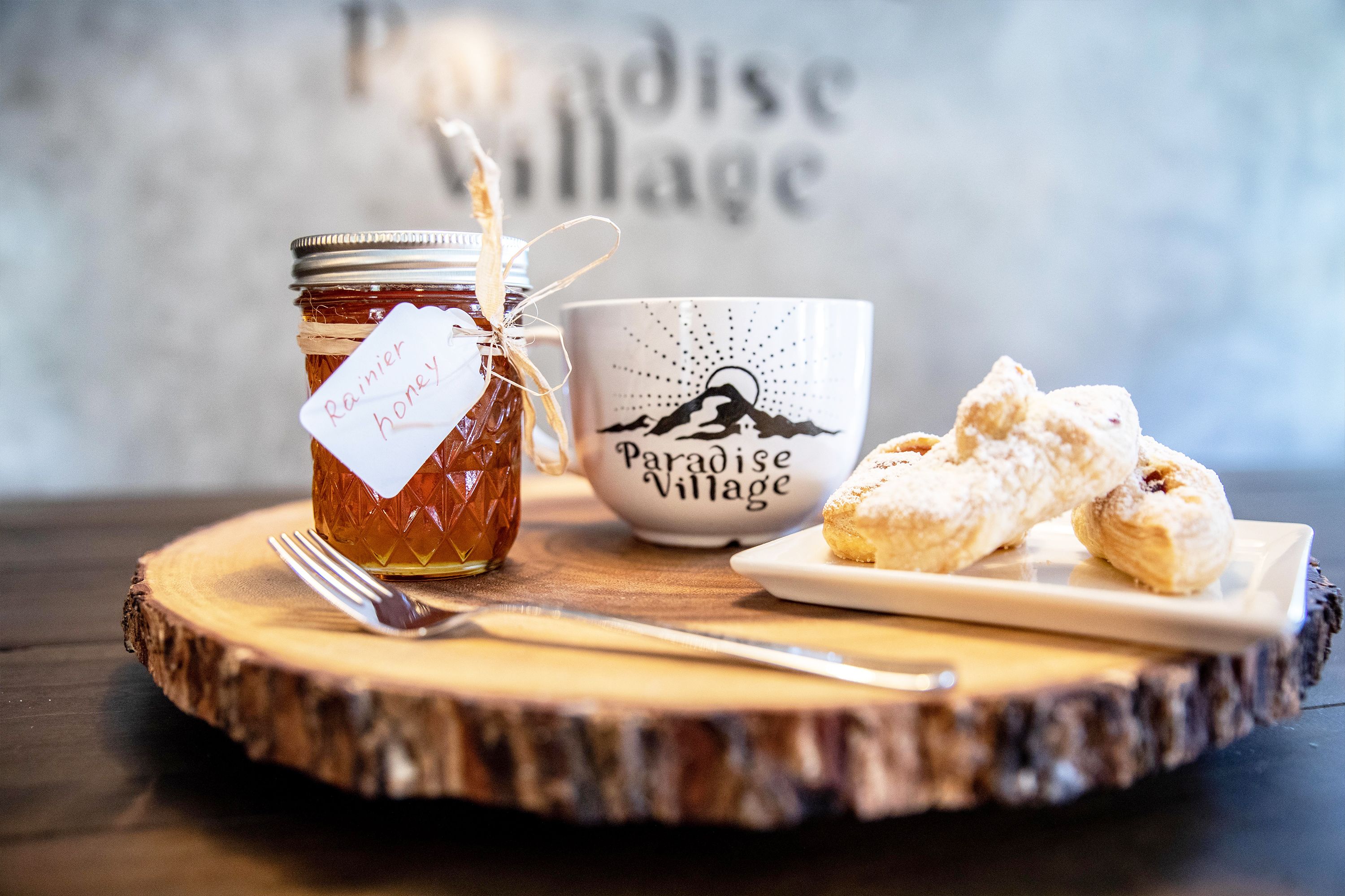 A jar of honey, a mug with a mountain design, and pastries on a wooden board.