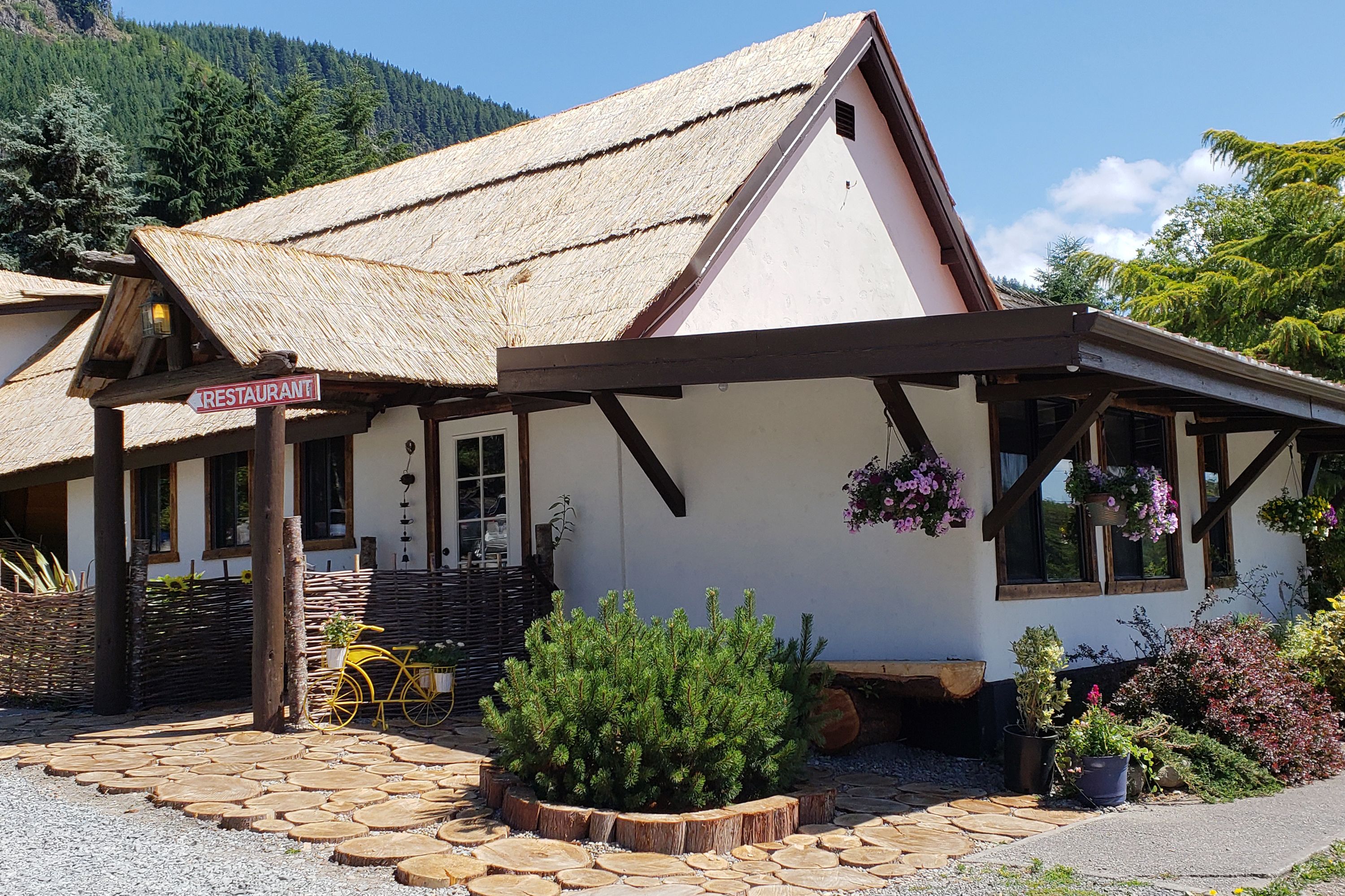 Un edificio rustico con un tetto di paglia, un’insegna che indica un ristorante e una bicicletta di legno parcheggiata fuori.