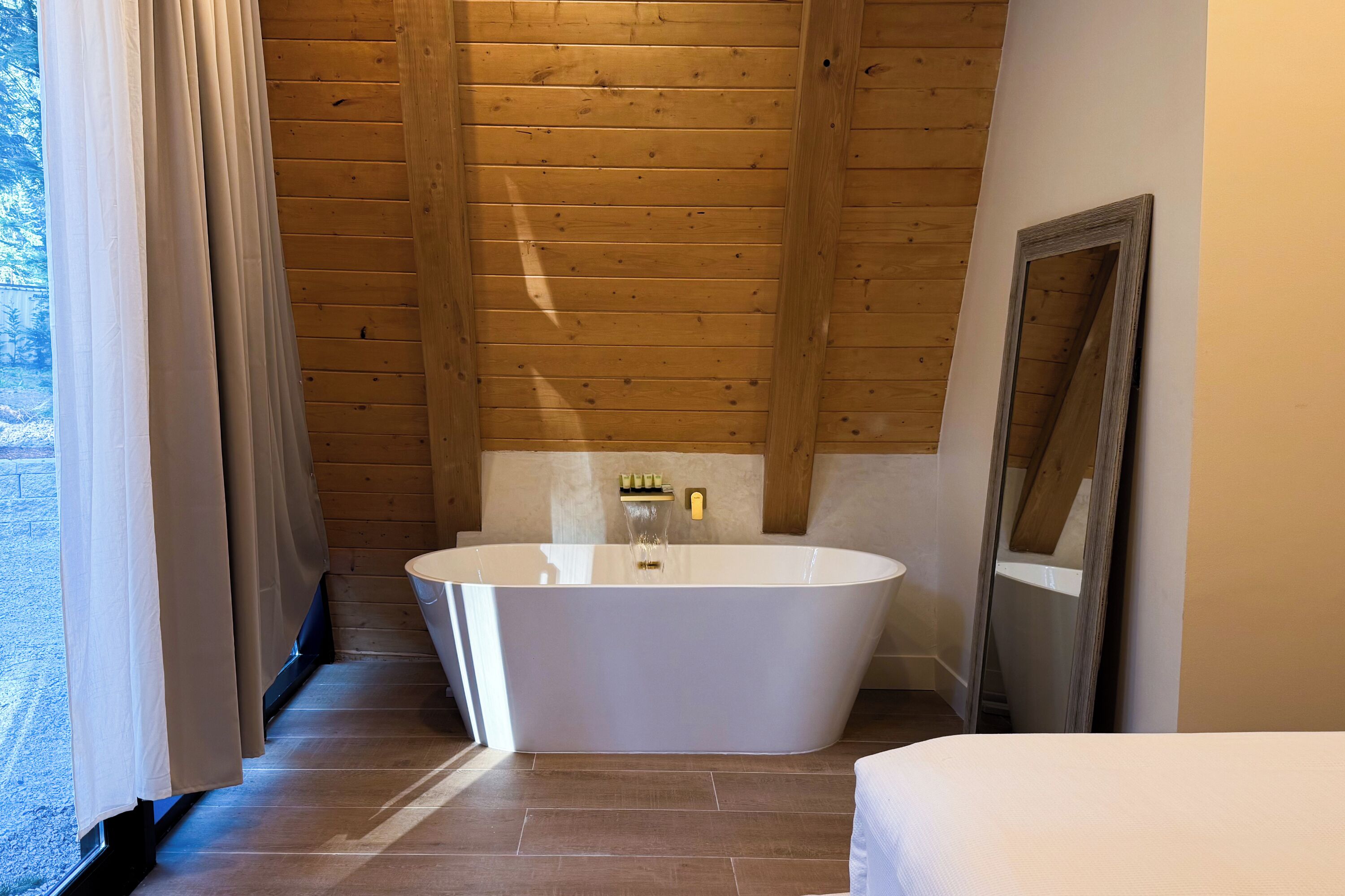 A modern bathroom with a freestanding bathtub, wooden panel walls, and a large mirror.