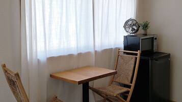 A small room with a wooden table and two woven chairs, a black refrigerator, and a microwave on top of it.