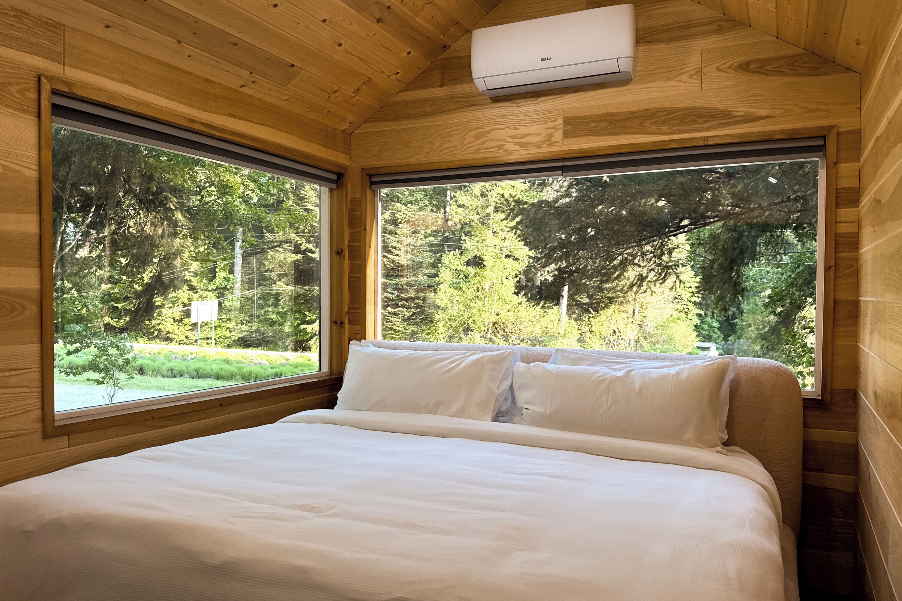 A wooden cabin bedroom with a bed, large windows, and an air conditioning unit.