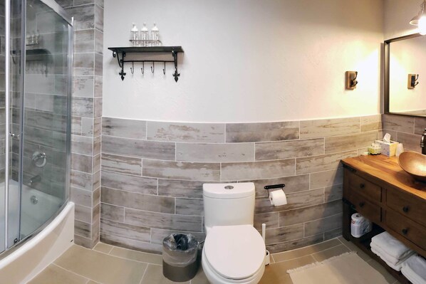 Un baño con ducha de vidrio, inodoro y tocador de madera con lavabo.