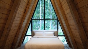 A bedroom with a bed centered under a large window, wooden walls, and a sloped ceiling. - Paradise Village Hotel (Ashford)