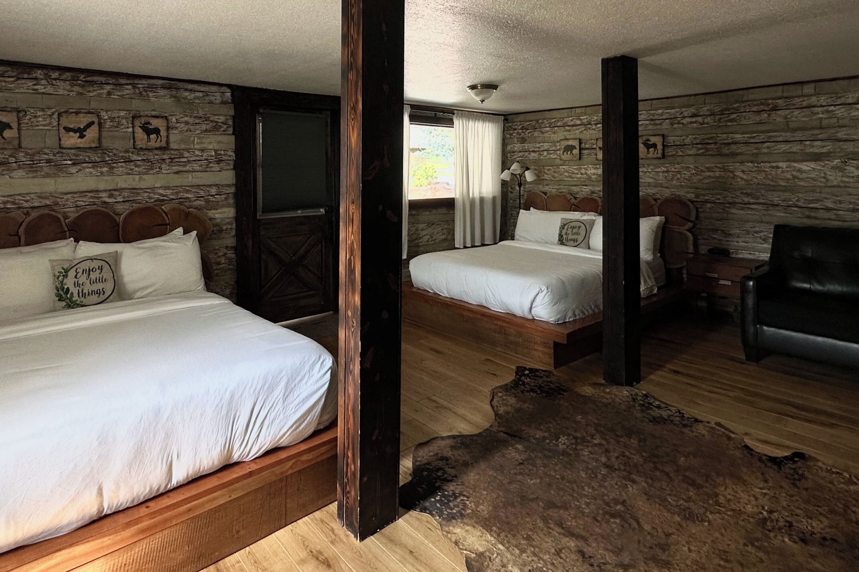 Ein Zimmer mit zwei Betten, Holzwänden, einem großen Fenster, einem Ledersessel und Holzboden.