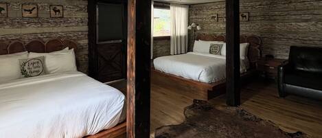 Ein Zimmer mit zwei Betten, Holzwänden, einem großen Fenster, einem Ledersessel und Holzboden.