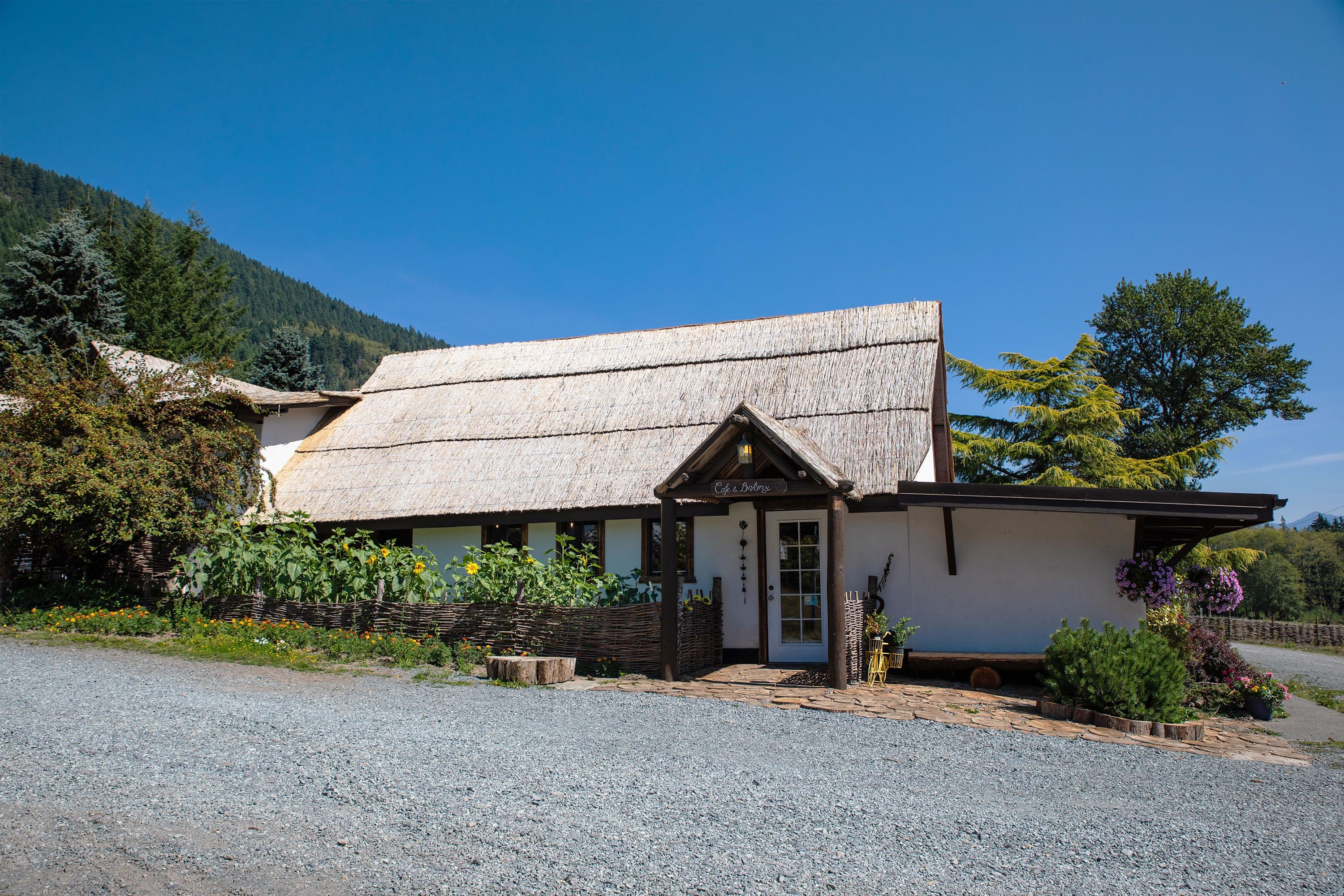 Un edificio rustico con tetto di paglia, un portico in legno e un cartello con la scritta 'Cafe Dolci'.