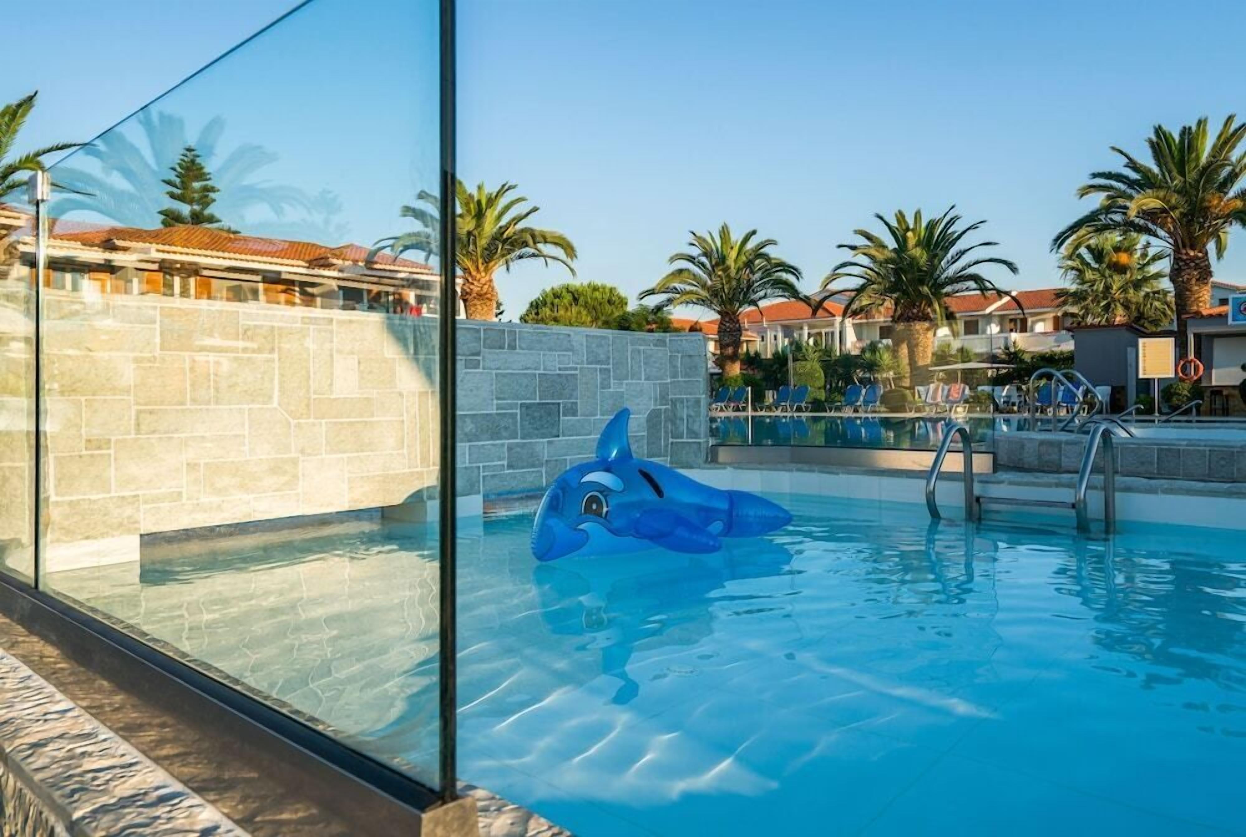 A swimming pool with a dolphin float, stone walls, and palm trees.
