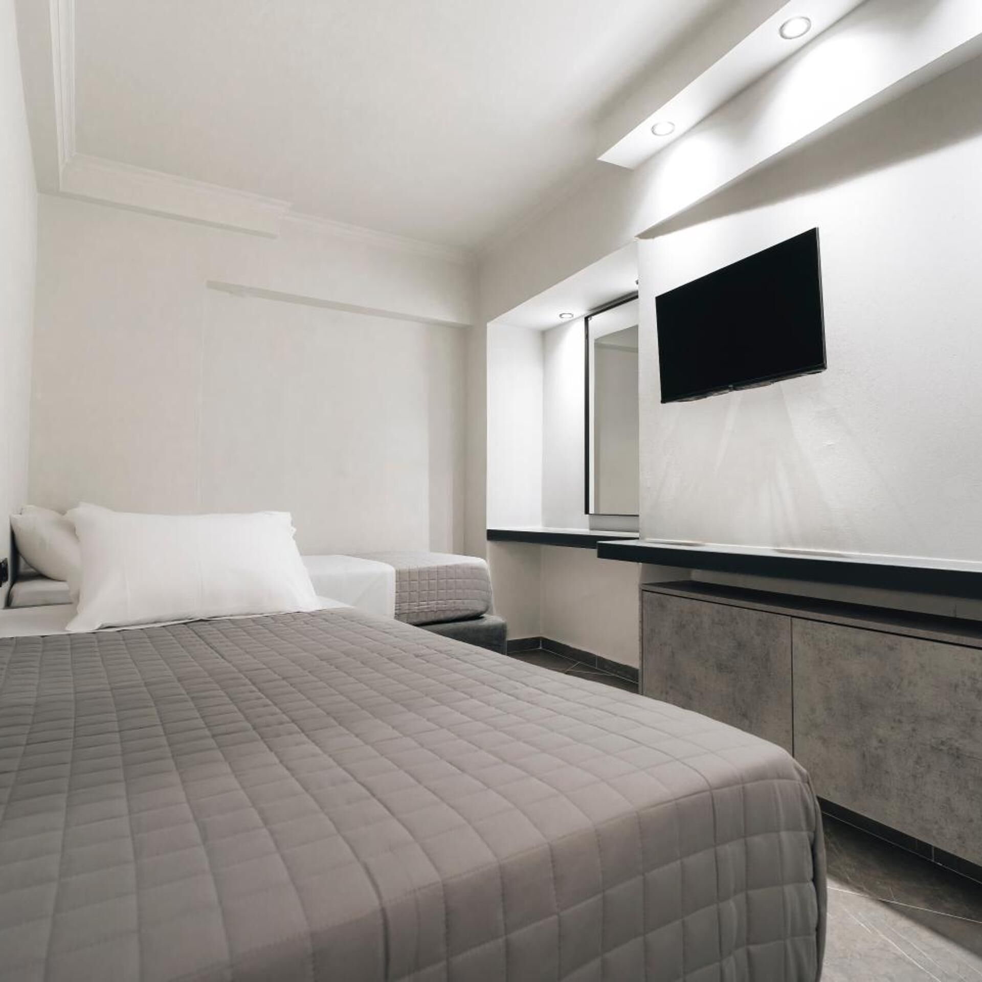 Ein modernes Hotelzimmer mit Bett, Nachttisch, Spiegel und einem an der Wand befestigten Fernseher.