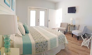 A bedroom with a bed, two doors, a chair, a small table, and a TV on the wall.