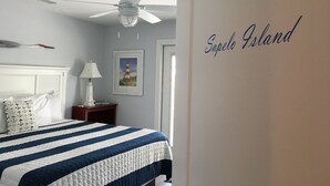 Ein Schlafzimmer mit Bett, Deckenventilator, Nachttisch, Lampe, gerahmtem Bild und einer Wand mit dem Schriftzug 'Sapelo Island'.