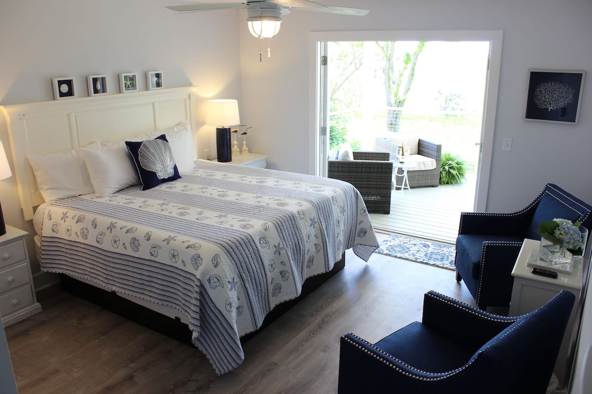 A bedroom with a bed, nightstands, a chair, and a view of the outdoors.