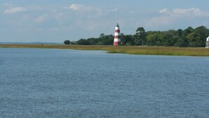 Ein Leuchtturm an einem ruhigen Gewässer, mit einer grünen Wiese und Bäumen im Hintergrund.