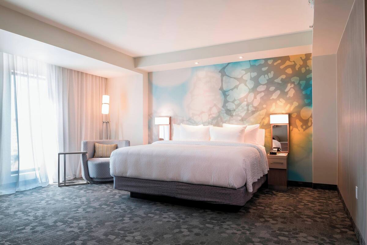 A hotel room with a large bed, a chair, a nightstand, and a wall with a textured design.