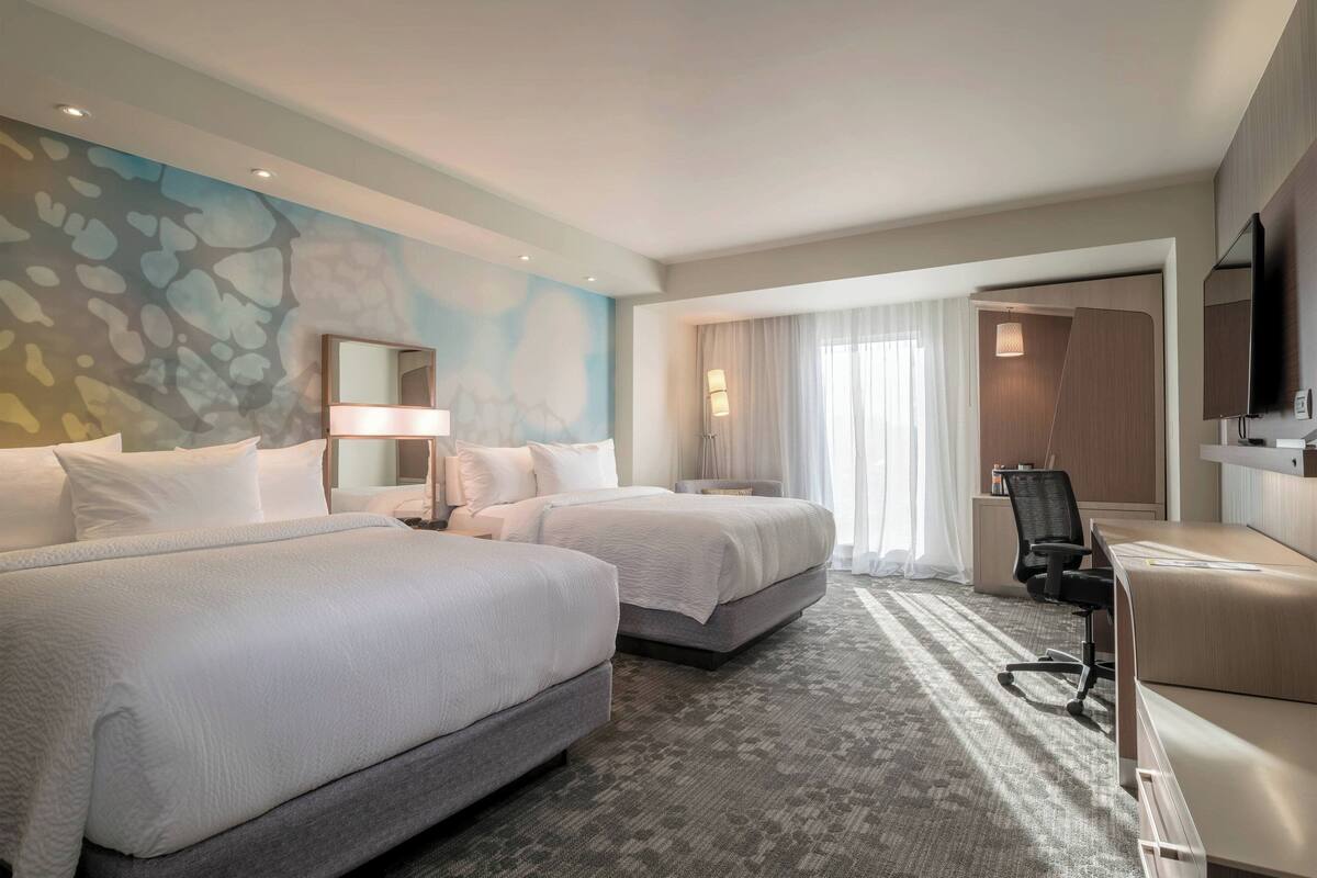 A hotel room with two beds, a desk, a chair, a TV, and a bathroom with a shower and toilet.