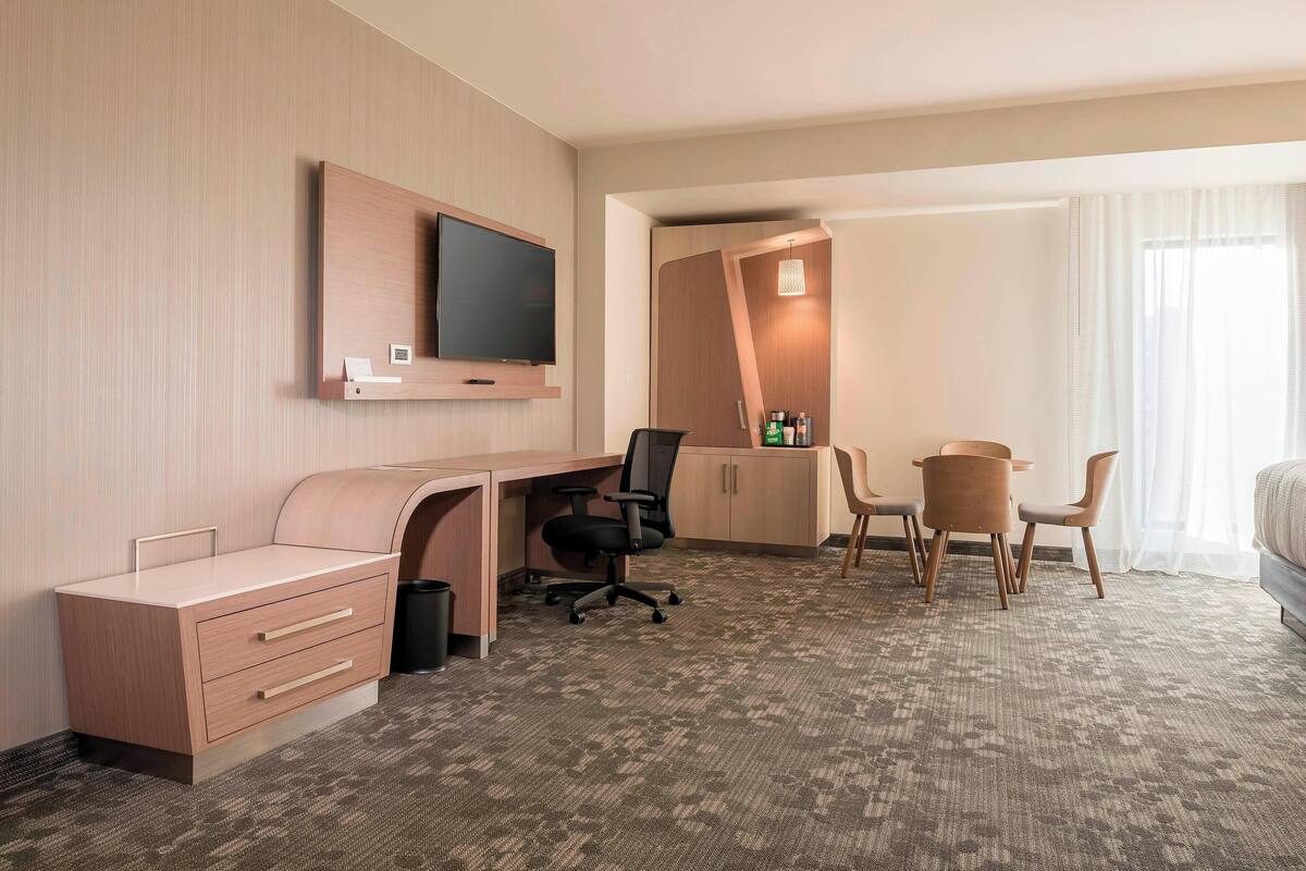 A hotel room with a wooden desk, a television, a chair, a small table, and a bed.