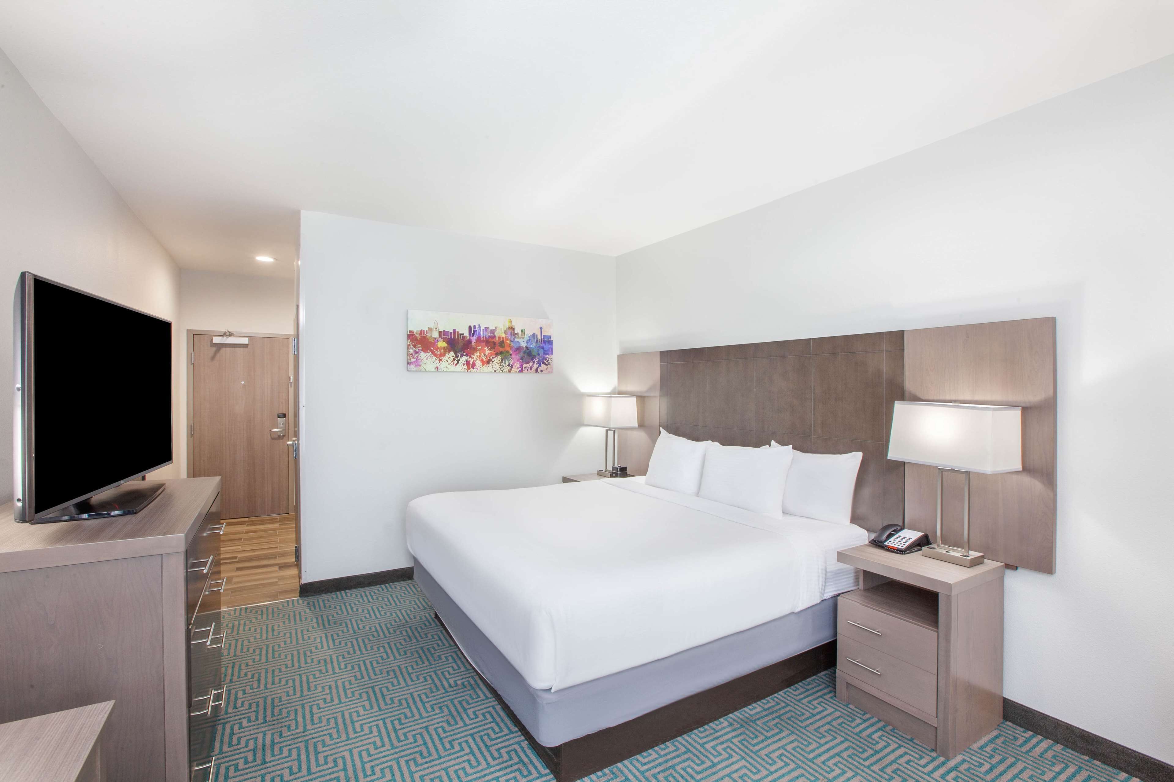 A hotel room with a large bed, a flat-screen TV, a desk with a lamp, and a telephone.