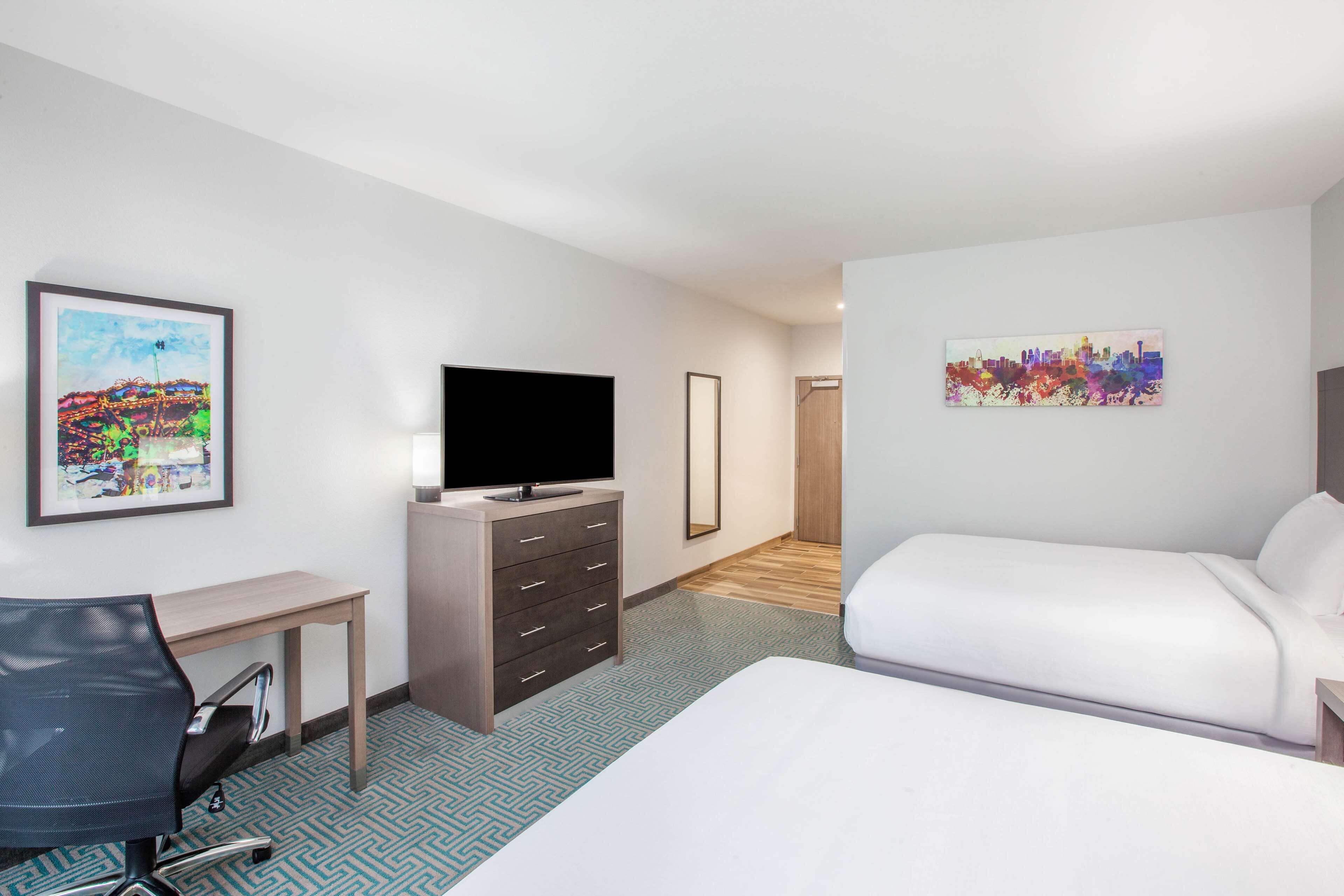 Ein Hotelzimmer mit einem Bett, einem Schreibtisch mit Stuhl, einem Fernseher und zwei Bildern an den Wänden.