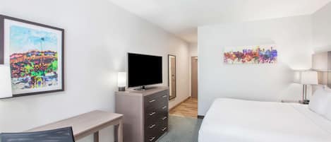 A hotel room with a bed, desk, TV, and artwork on the walls.