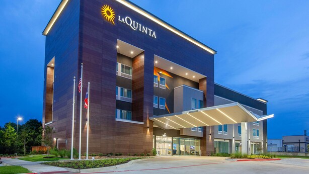 Un hotel moderno con un llamativo letrero de 'La Quinta', un acceso cubierto e izado un mástil con banderas.